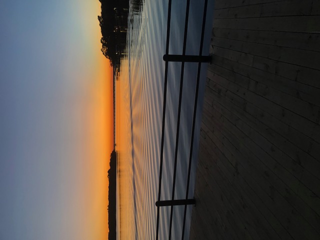 Sunset over Cedar Creek Lake, viewed from a boathouse deck with a railing in the foreground